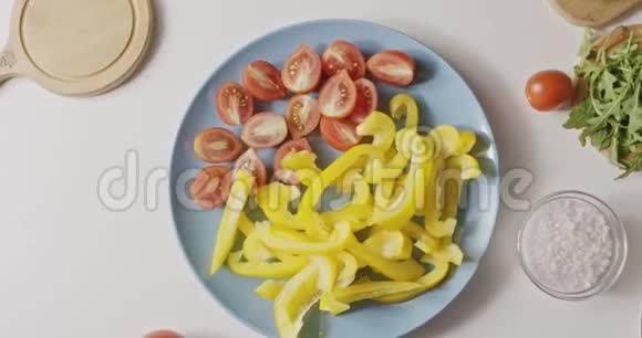 将成熟的红西红柿和黄色辣椒切成薄片放在白色桌子上的蓝色陶瓷盘子上上面有有机天然成分视频的预览图