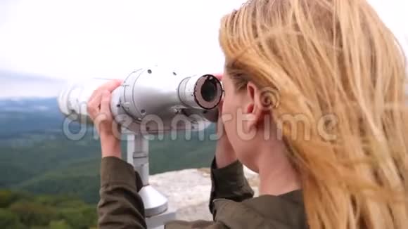 一个金发女郎透过山顶上的望远镜看4k慢镜头视频的预览图