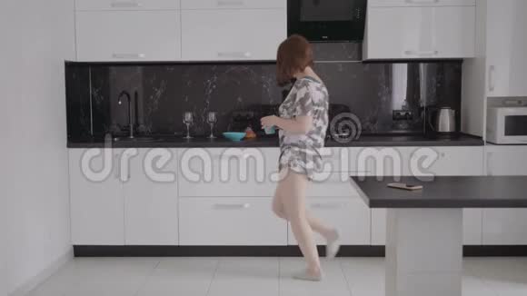 有趣的年轻女人早上穿着睡衣在厨房跳舞视频的预览图