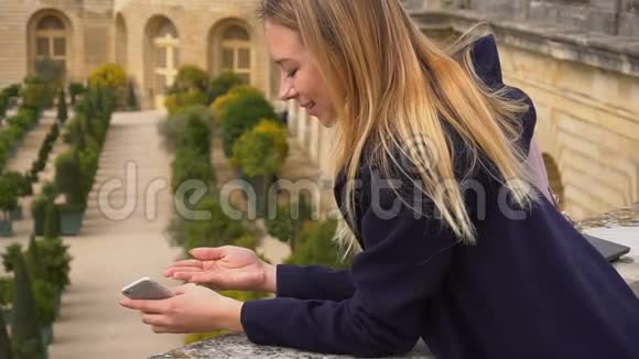 迷人的女人站在智能手机和保持瓢虫与凡尔赛背景视频的预览图