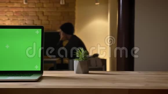 通过相机拍摄笔记本电脑的特写镜头办公室的办公桌上有绿色屏幕员工在室内视频的预览图
