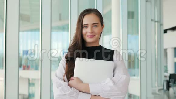 一位微笑的年轻女子站在灰色背景下的笔记本电脑上的肖像一位快乐的工人女商人年轻视频的预览图