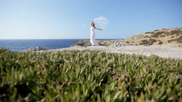 一位快乐的新娘站在海边戴着一层在风中飘扬的婚纱幸福婚姻的概念视频的预览图