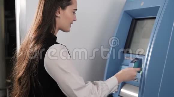 年轻女子在自动取款机上插入一张信用卡美丽的女孩在购物中心机场候机楼上无触点的NFC银行视频的预览图