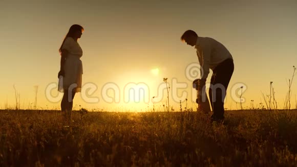 年轻漂亮的家庭在田野里和孩子在夕阳下一个小孩子学会和爸爸妈妈一起散步慢动作视频的预览图