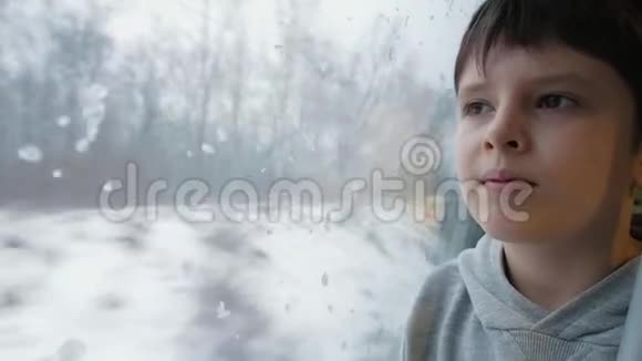 坐在客车里的男孩透过火车车窗向外望到白雪覆盖的田野和树木视频的预览图
