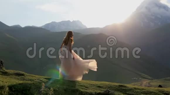 穿着美丽裙子的女孩在群山和夕阳的背景下视频的预览图
