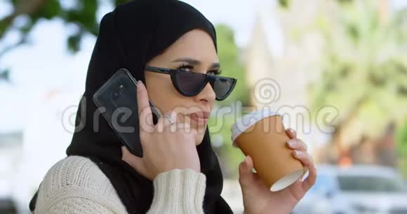 戴头巾的女人一边喝咖啡一边用手机说话视频的预览图