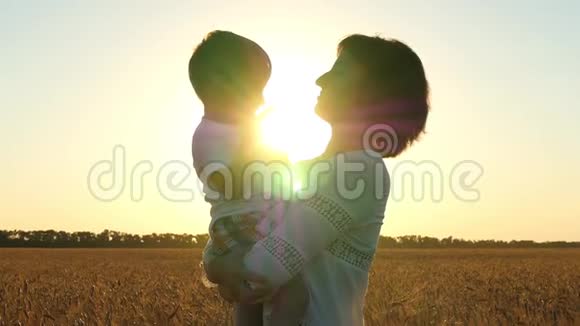 一位快乐的母亲在夕阳的背景下把孩子抱在麦田的怀里快乐的孩子抚摸他视频的预览图