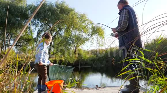 小孙子和爷爷在湖里钓鱼天气很好在树和草之间钓鱼视频的预览图