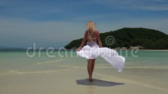 穿着白色裙子在热带沙滩散步的白种人年轻女子视频的预览图