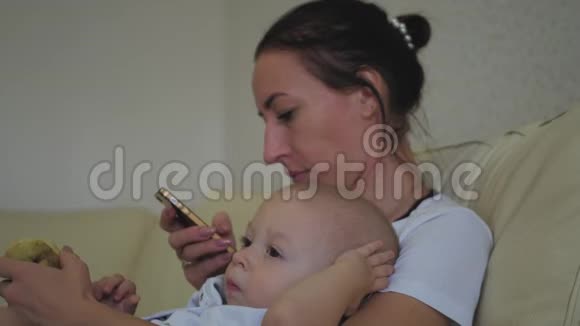家庭技术母性和人的概念幸福的母亲小男孩躺在沙发上智能手机上视频的预览图
