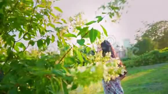 年轻女子在花园里的一棵绿树上嬉戏玩耍一个微笑的黑发女人的肖像两颊酒窝视频的预览图