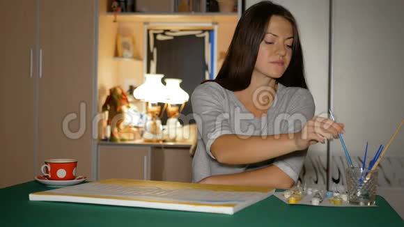 开始的艺术家把她在家里的第一幅大画画在桌子上女孩拿着她的手一支干净的刷子选择视频的预览图