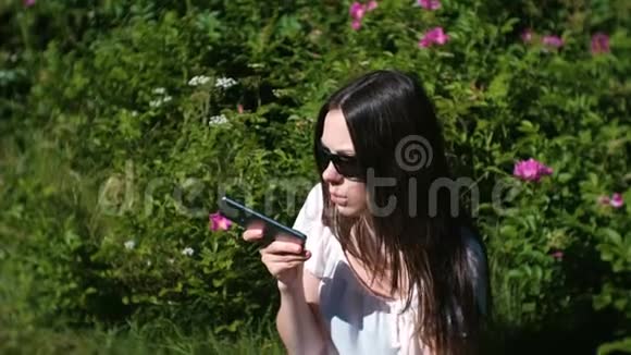 阳光明媚的一天美丽的黑发女人坐在公园里在手机上记录了一条语音信息视频的预览图