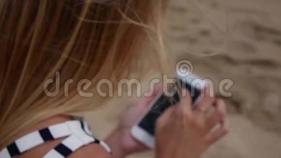 一位身材苗条金发碧眼的年轻美女身穿黑白连衣裙坐在沙滩上用的是一种视频的预览图