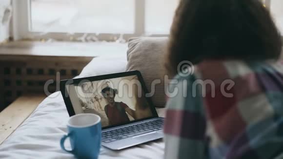 可爱的年轻女性躺在床上与朋友用笔记本电脑摄像头在线视频聊天视频的预览图