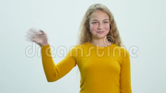 一个女孩站在演播室的白色背景上挥舞着她的手视频的预览图