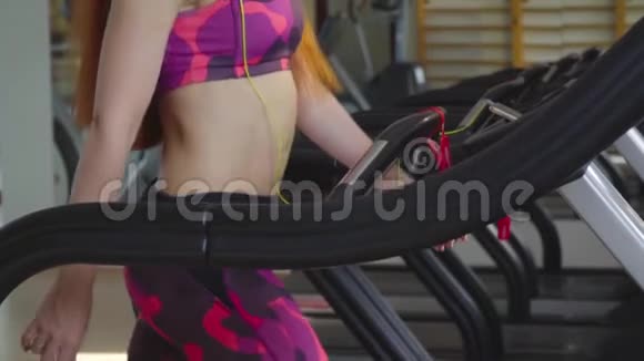一个留着红色长发的女人在跑步机上听音乐听耳机音乐慢动作视频的预览图