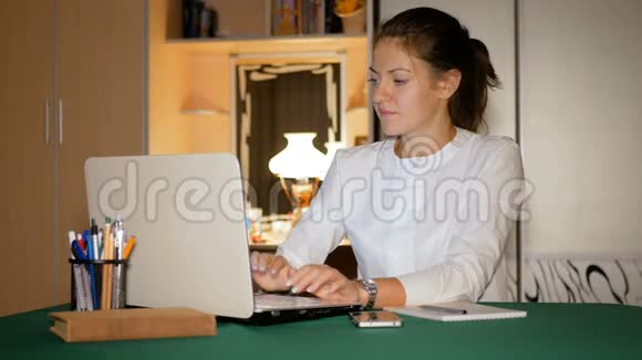 女孩自由职业者在温暖的家庭环境中为笔记本电脑工作布鲁内特把信息从屏幕写到视频的预览图