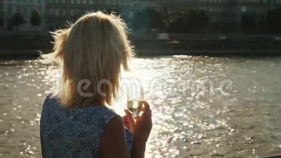 一个手里拿着玻璃杯的女人欣赏风景从后面看船上的船河上的游船视频的预览图