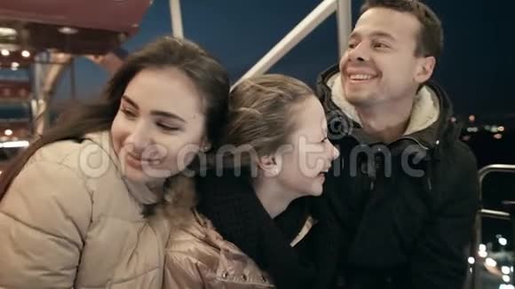 年轻的一家人一起在摩天轮上拥抱晚上在午餐会上父亲母亲和女儿视频的预览图