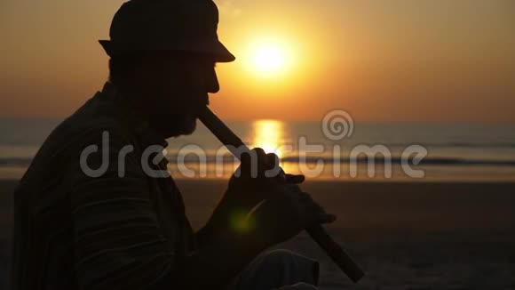 日落时分在沙滩上吹竹笛的老人剪影视频的预览图