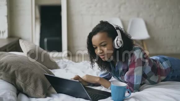 年轻卷曲的非裔美国妇女躺在床上一边在笔记本电脑上听音乐视频的预览图
