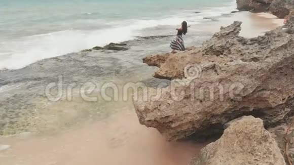 印度尼西亚女孩享受生活伸出双手在巴厘岛的岩石海岸视频的预览图
