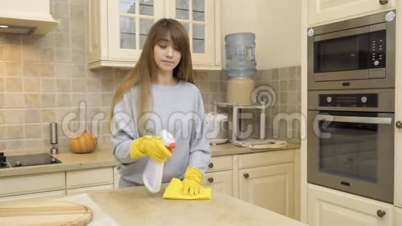漂亮的女孩戴着防护手套在厨房用洗涤剂清洁桌子视频的预览图