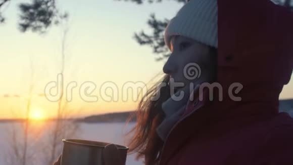 这位女游客正在日落时分在白雪皑皑的冬林里喝热水瓶里的茶视频的预览图