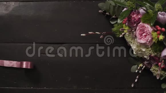 两条丝质的粉色缎带舒展在漆黑的木质表面一束美丽的花束在一个框架内慢动作视频的预览图