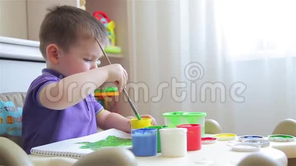 坐在桌子上男孩用彩色颜料画画视频的预览图