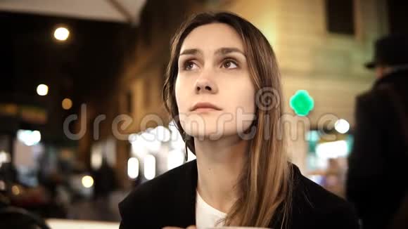 年轻的美女坐在市中心的咖啡馆里晚上独自拿着杯子喝咖啡视频的预览图