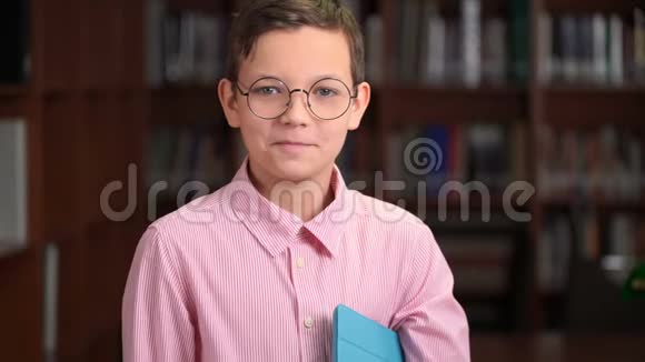一张可爱的小学生的画像他拿着平板电脑站在图书馆的书架附近视频的预览图