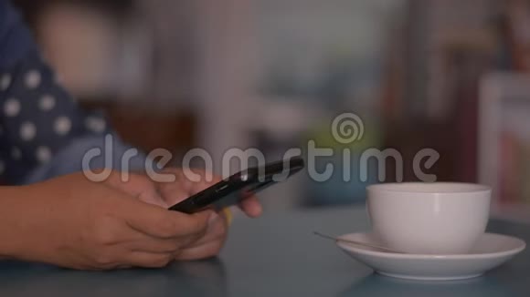 女人用智能手机在家里的桌子上喝一杯咖啡打字短信视频的预览图