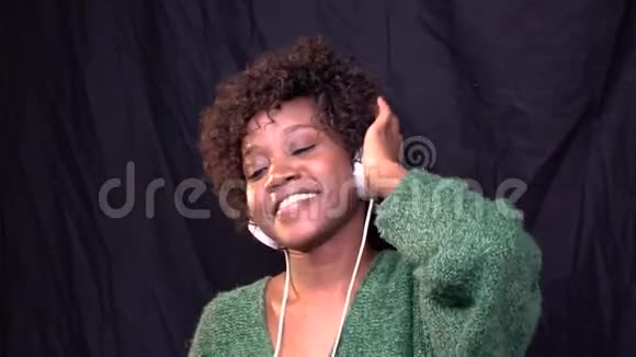 快乐的非裔美国女人戴着白色耳机在演播室里跳舞听音乐有点慢动作视频的预览图