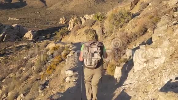在莫哈韦沙漠后景中沿着小径下山的活跃妇女视频的预览图