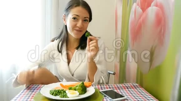 一个穿着白色外套的好女孩手里拿着叉子和一块煮好的西兰花黑发女人在玩视频的预览图
