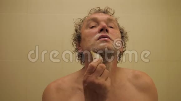 一个英俊的成年人照镜子刮胡子的肖像视频的预览图