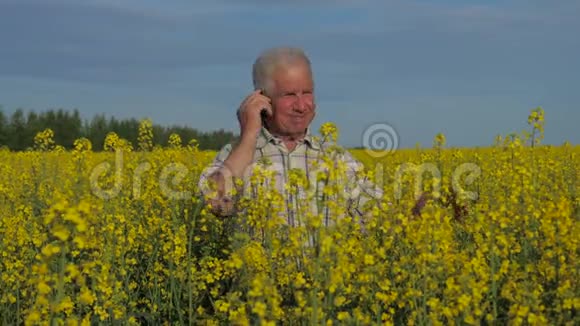 一个农民站在一片盛开的黄色油菜花田里打电话视频的预览图