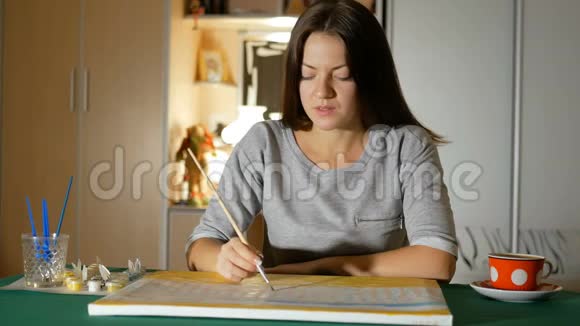 一位年轻女子在家里的桌子上画了一幅画晚上为有才华的青年休闲灯照在背景上视频的预览图