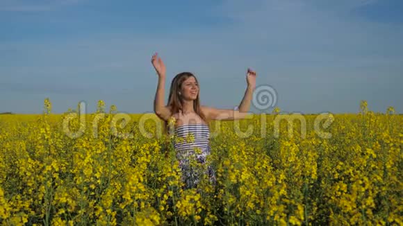 一个可爱的女孩在黄色的田野里挥舞着双手欢迎的肖像视频的预览图
