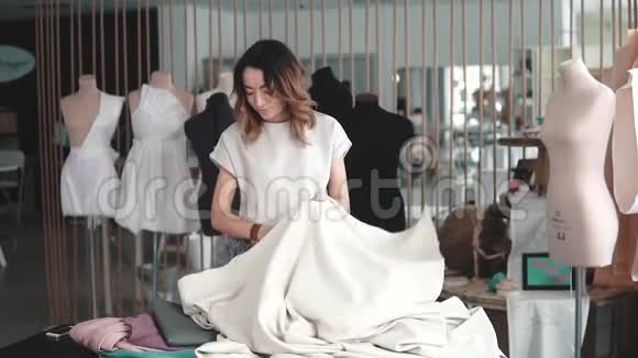 在缝纫室工作的年轻女子女孩设计师的衣服在桌子上碎布裁缝在他的助手工作视频的预览图