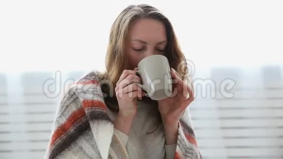一个简单的女人喝着裹在温暖毛毯里的茶视频的预览图