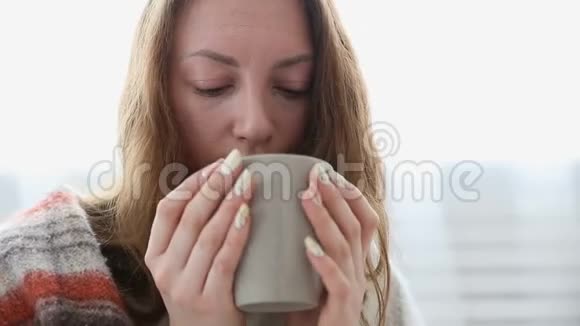一个简单的女人喝着裹在温暖毛毯里的茶视频的预览图