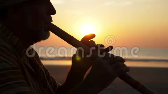 日落时分在沙滩上吹竹笛的老人剪影视频的预览图