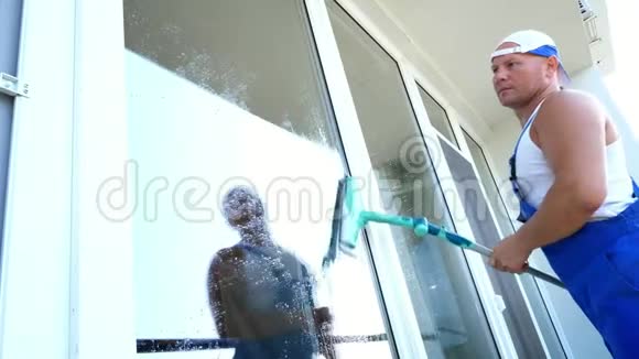白人英俊男子清洁服务工人穿着蓝色工作服戴着一顶帽子擦擦擦窗户视频的预览图