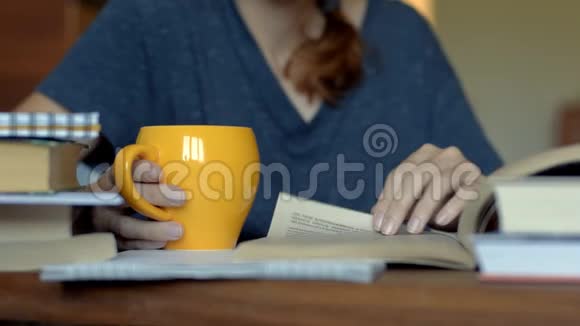 一个拿着橙色杯子的年轻女子在桌旁看书视频的预览图