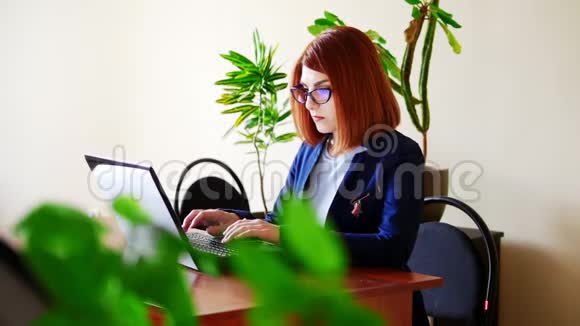 戴眼镜的年轻女子在办公室的笔记本电脑上打字视频的预览图